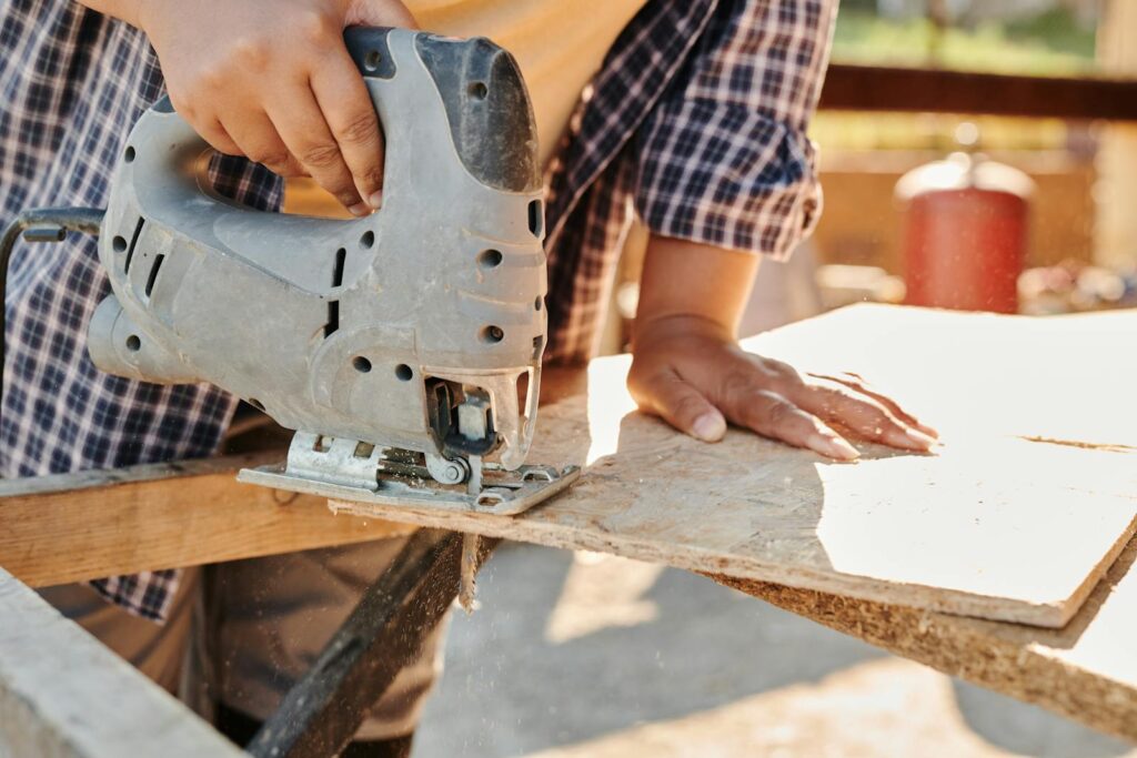 Person Holding Gray Metal Tool Cutting Plywood