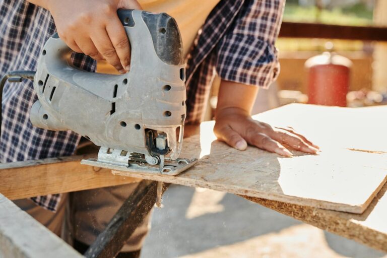 Person Holding Gray Metal Tool Cutting Plywood