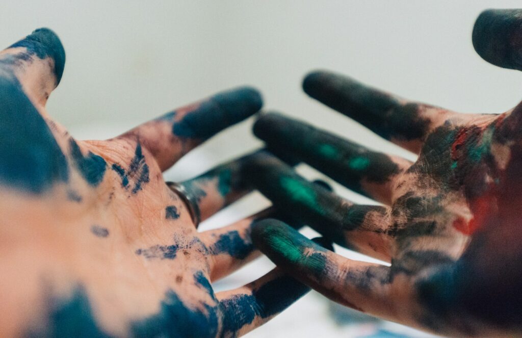 person hand with green and blue paint while painting on laminate flooring